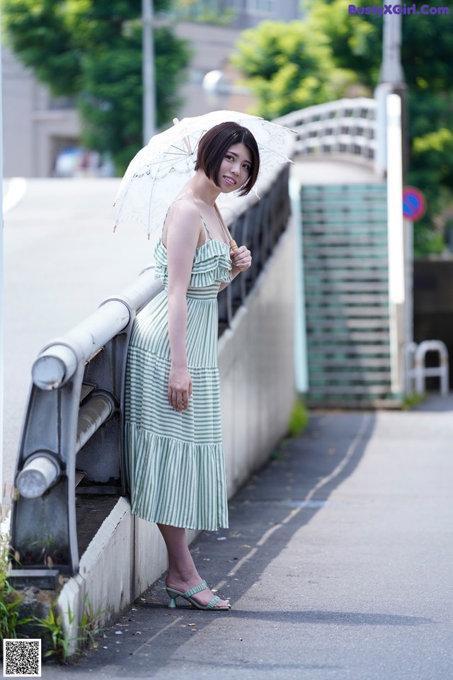 A woman in a green and white striped dress holding an umbrella.