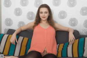 A woman in a blue shirt and skirt sitting on a bed.