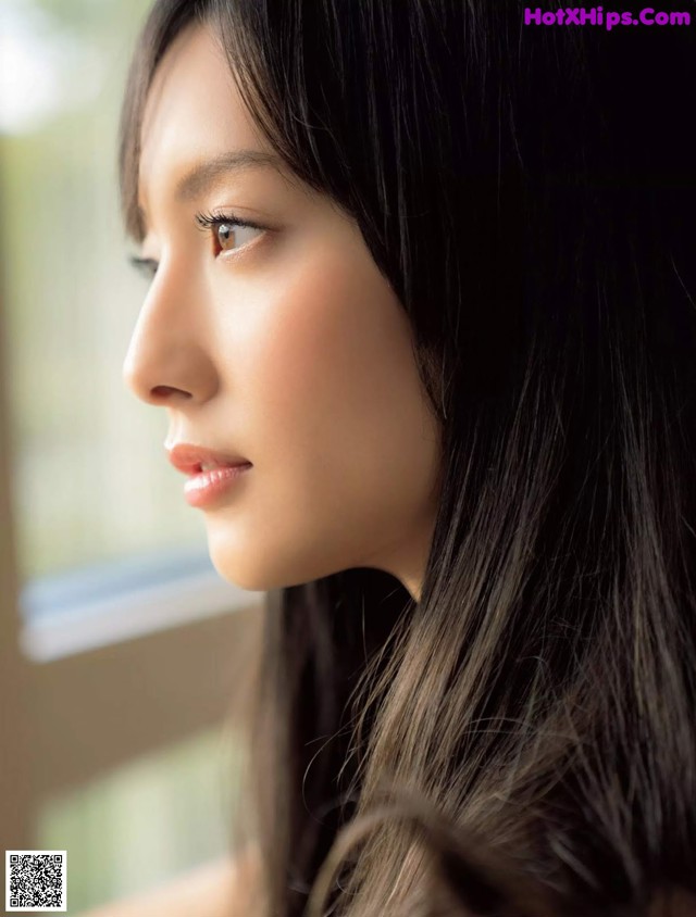 A woman with long black hair looking out a window.