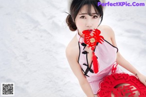 A woman in a pink dress holding a red fan in the snow.
