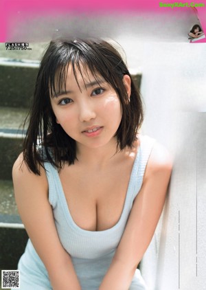 A woman in a blue tank top sitting on a bed.