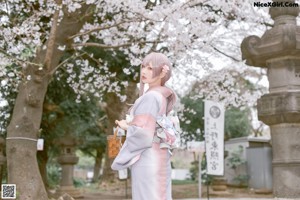 A woman in a pink kimono standing in front of a tree.