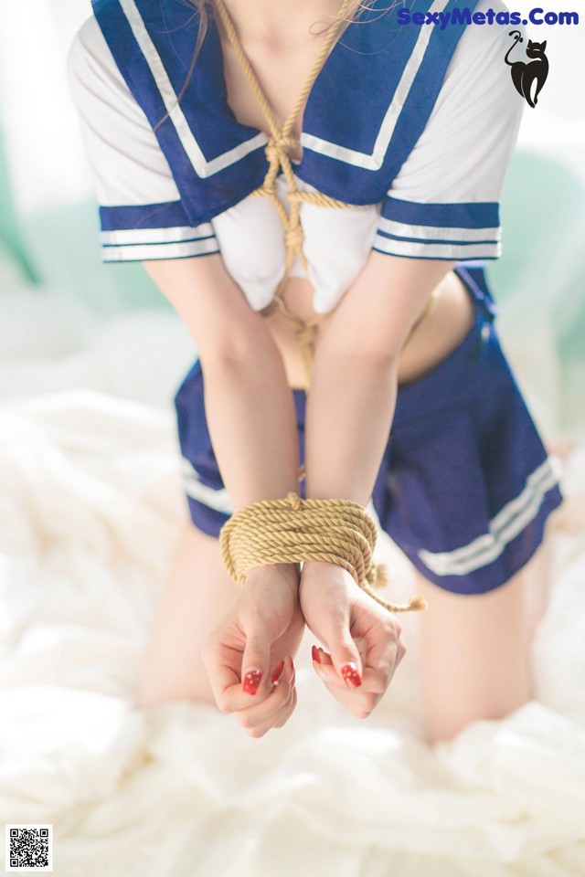 A woman in a sailor outfit tied up on a bed.