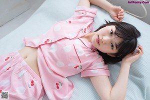 A woman in a pink polka dot pajamas sitting on a bed.