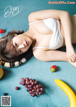 A woman in a white bikini sitting on the floor with fruit on her head.