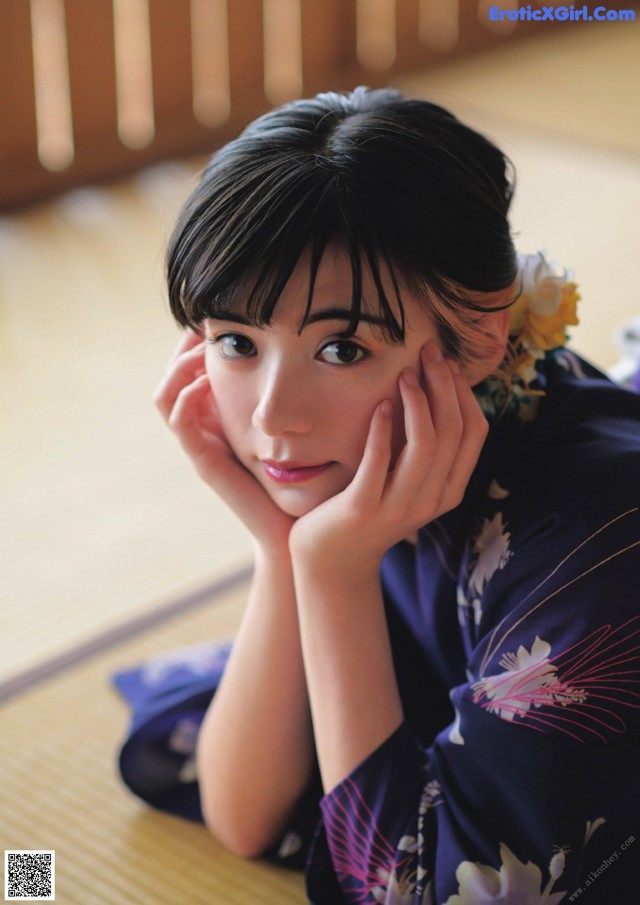 A woman in a kimono sitting on the floor with her hand on her chin.