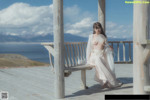 A woman in a white dress holding an umbrella in a field.