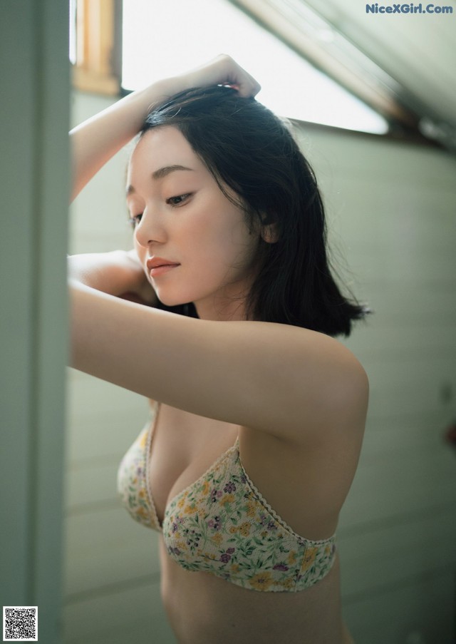 A woman in a floral bra and panties leaning against a window.