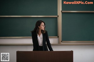 A woman sitting on top of a desk next to a blackboard.