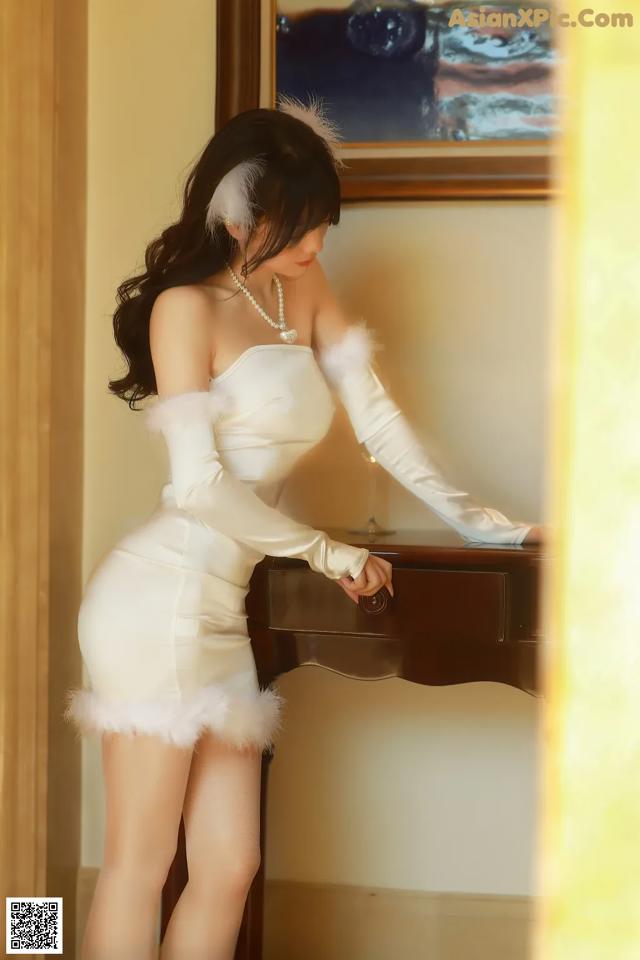 A woman in a white dress standing next to a piano.