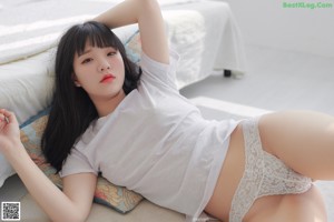 A woman laying on a bed wearing a white shirt and panties.