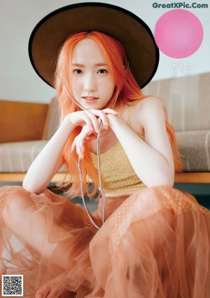 A woman with bright orange hair laying on a bed.